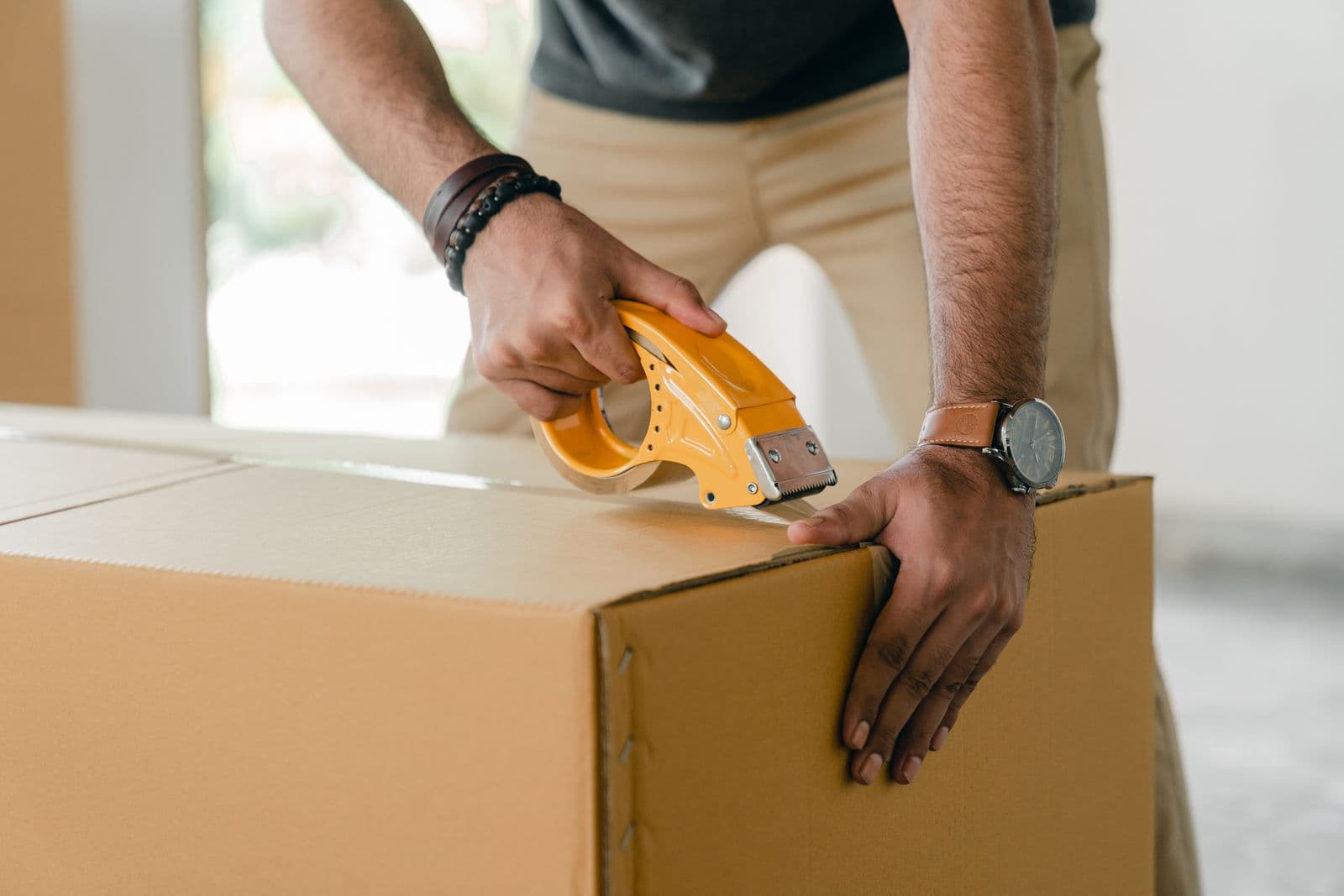 A person sealing a cardboard moving box with packing tape