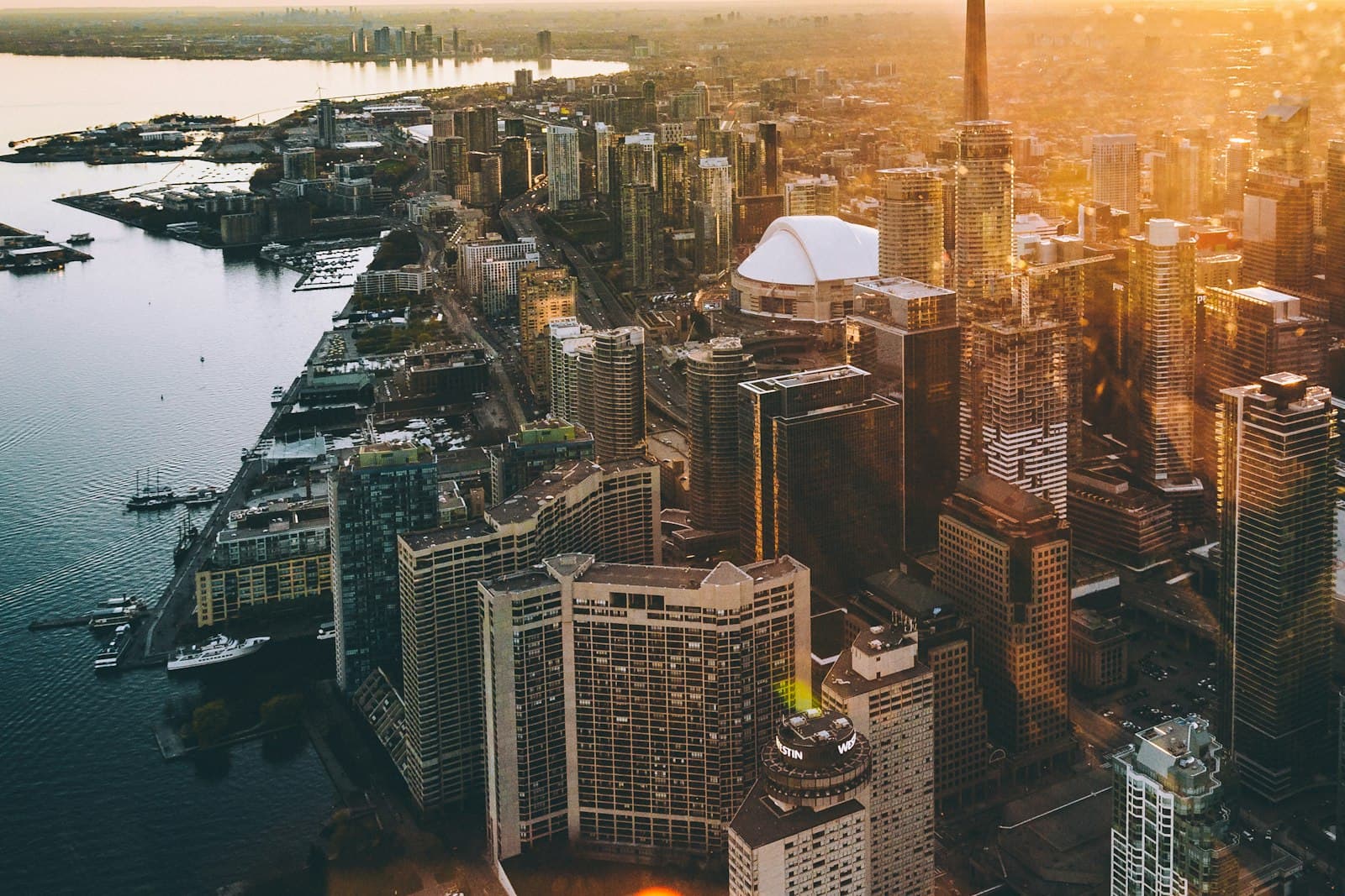 Downtown Toronto at sunset from the harbour, with condo towers, the CN Tower, and Rogers Centre along the waterfront