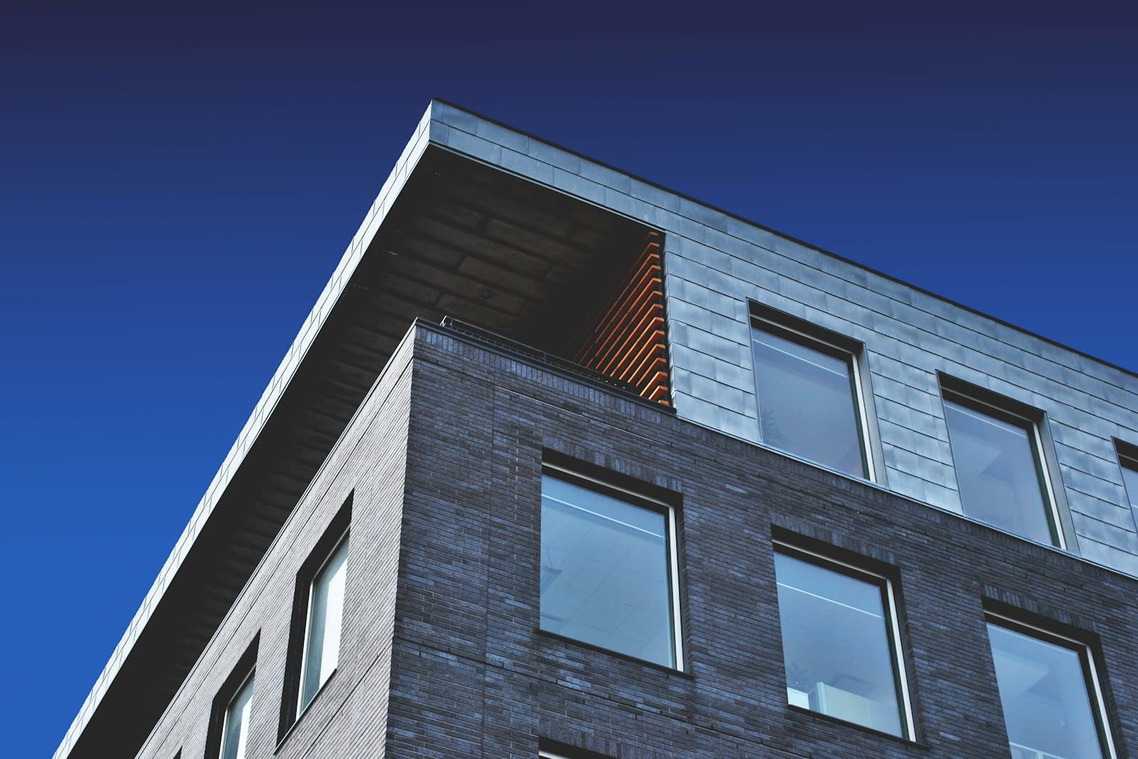 A modern brick and panel townhouse or low-rise building photographed from below against a blue sky