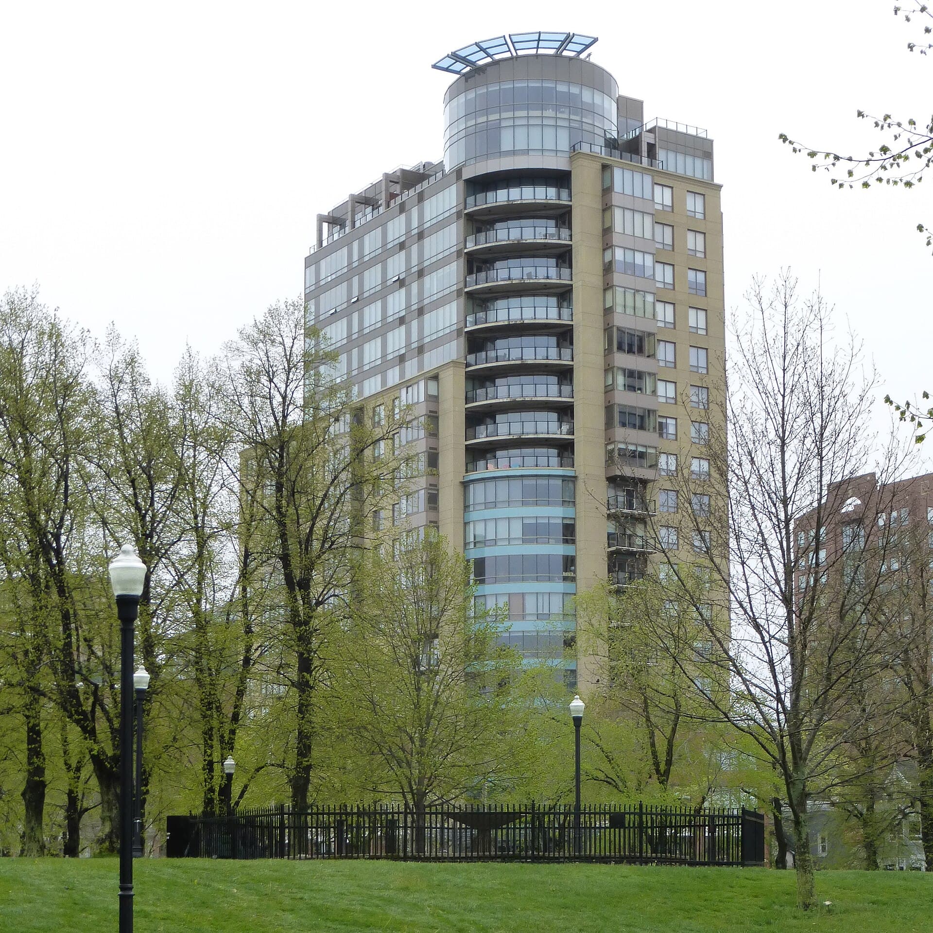 The Trillium, a curved condominium tower with a glass rooftop canopy, seen through trees in Halifax