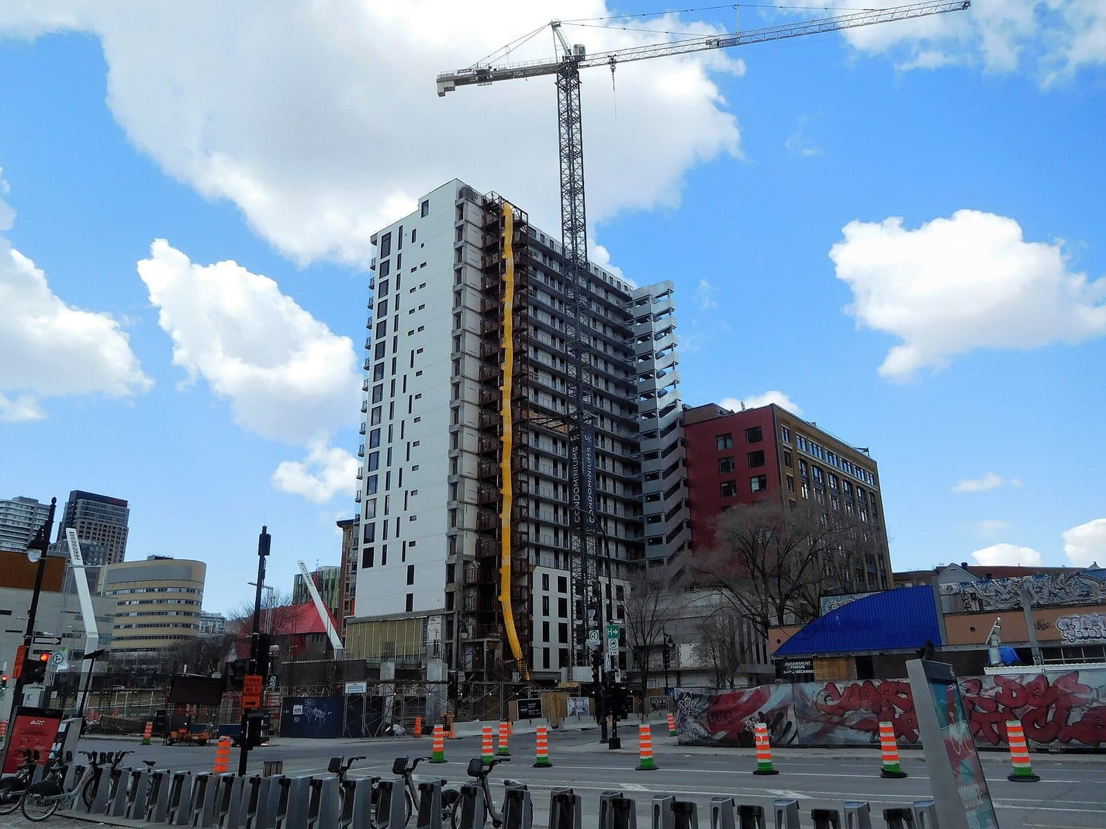 A white and glass condo tower with a crane, seen across a street