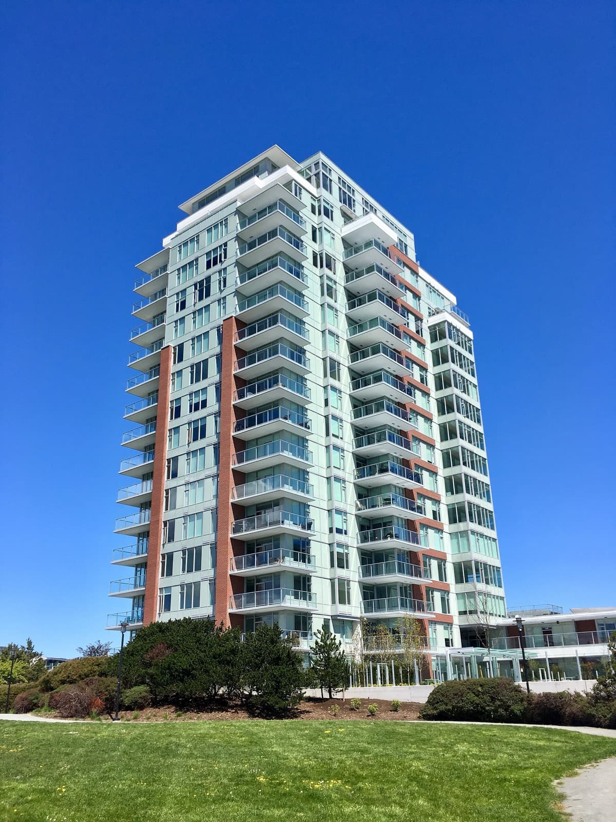 Encore, a 17-storey glass condo tower with orange accent columns beside a green lawn