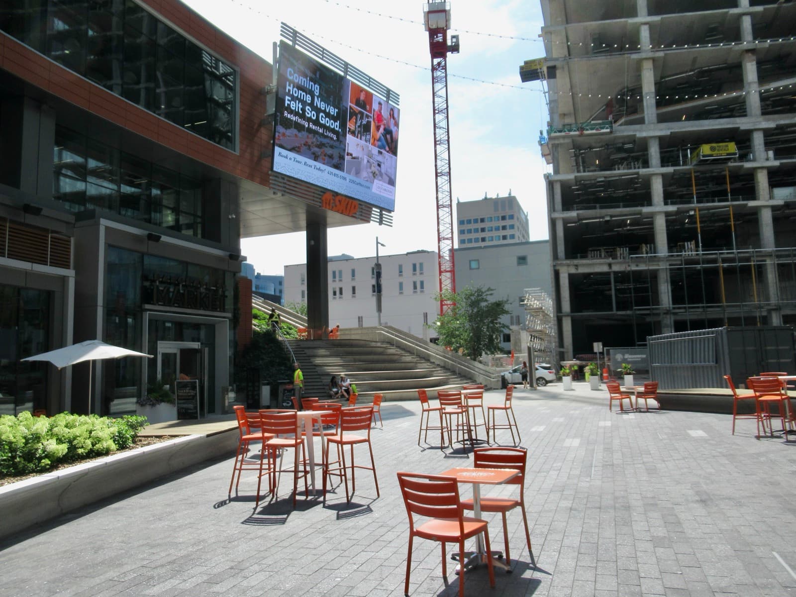 The plaza at True North Square with café seating and a tower crane behind
