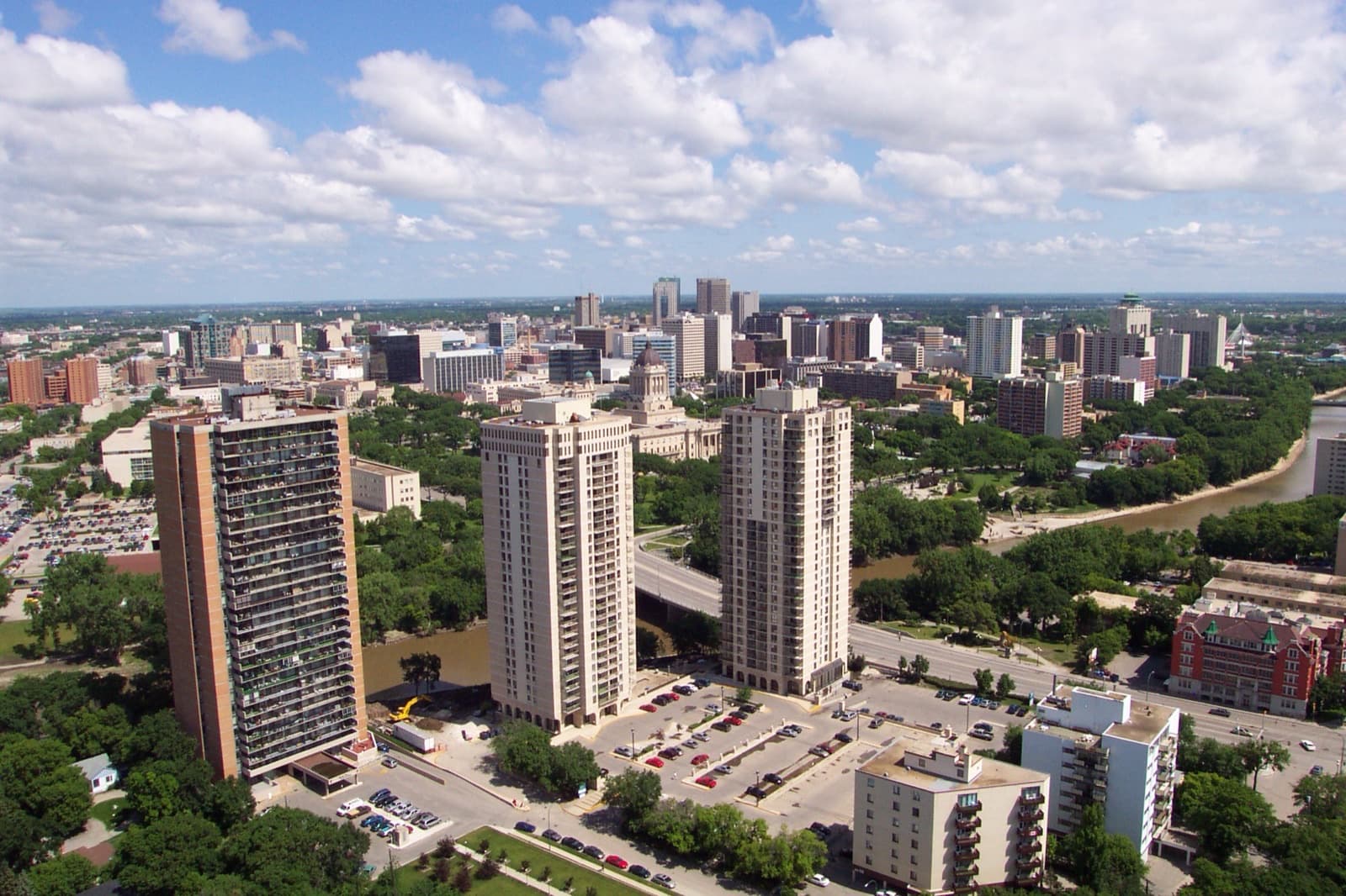 A wide view north over Osborne Village apartment towers and the Assiniboine River toward downtown Winnipeg