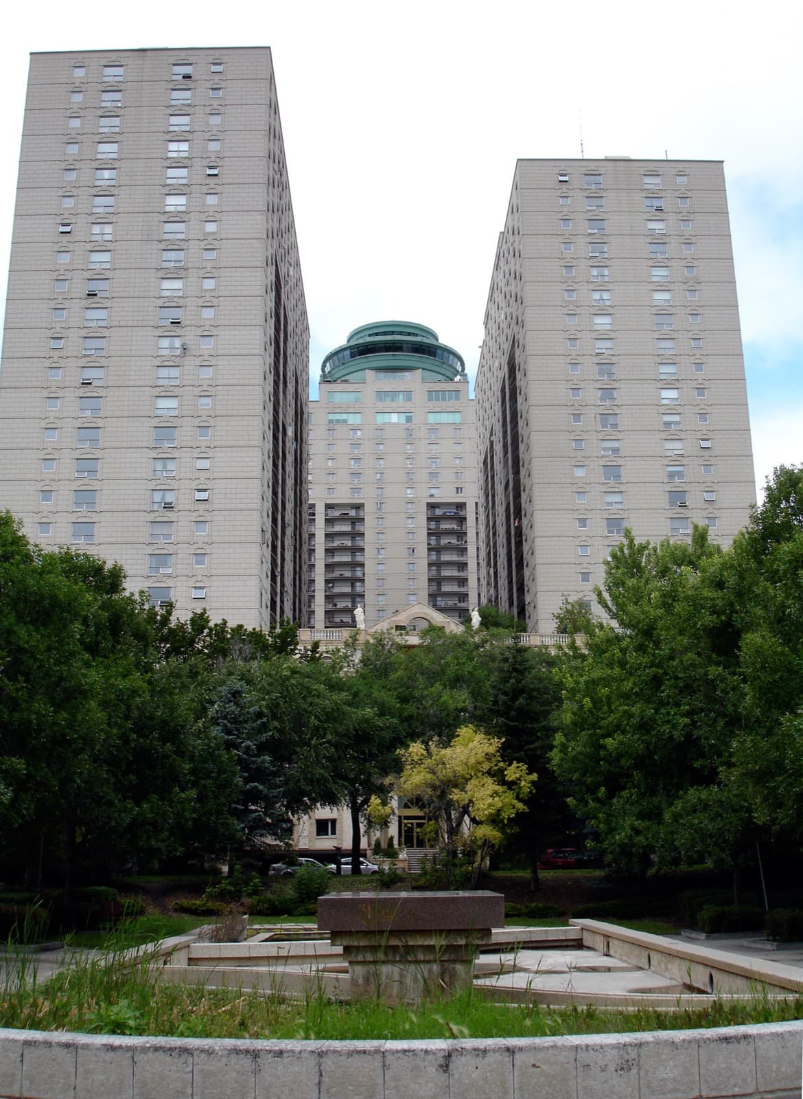 Two towers of Fort Garry Place seen from a garden, with the revolving restaurant between them