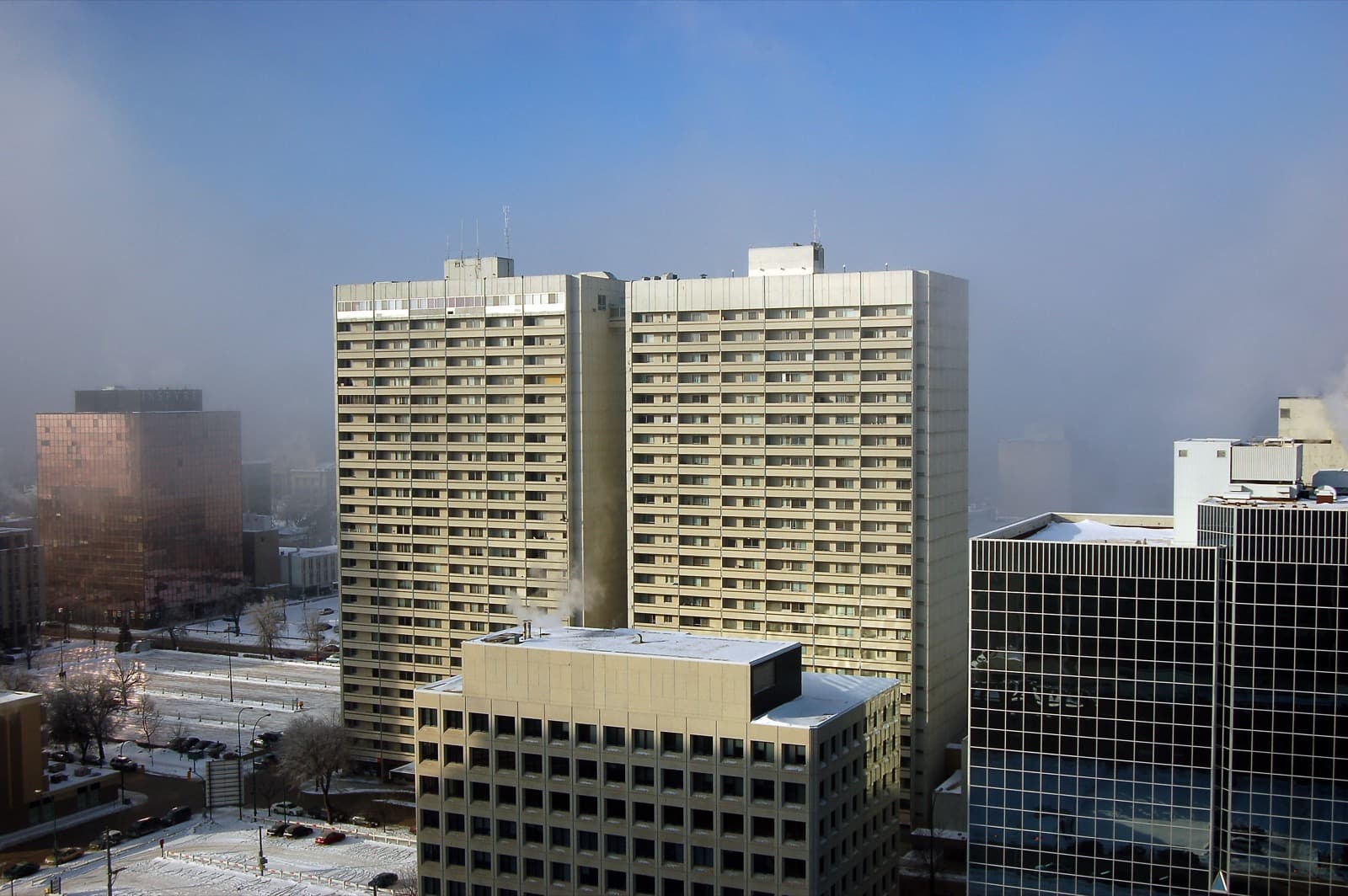 The twin concrete slabs of Holiday Towers in winter fog above downtown Winnipeg