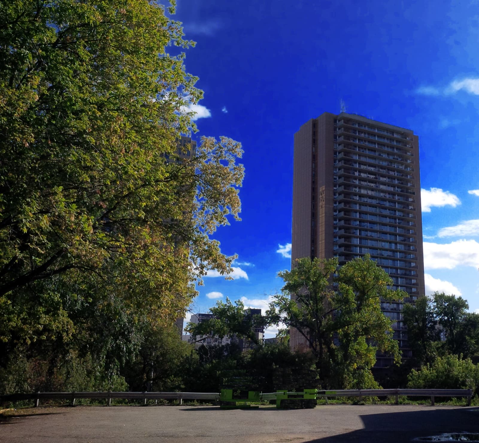 The slab tower of One Evergreen Place rising above trees on the Assiniboine River