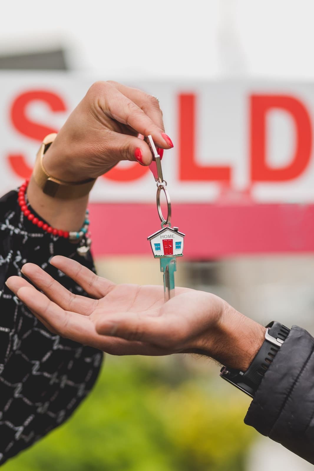 A house key being handed over in front of a SOLD sign